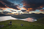 walker in front of the fjord and town of vetsmanna beneath a colorful sunset, streymoy, faroe islands, denmark