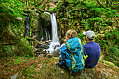 Mann und Frau beim Wandern blicken auf Wasserfall, Höllbach-Wasserfall, Albsteig, Schwarzwald, Baden-Württemberg, Deutschland