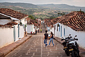 junges paar überquert steile Gasse mit Blick auf das fruchtabre Umland, Barichara, Departmento Santander, Kolumbien, Südamerika