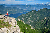 Mann beim Wandern steht auf Felsabsatz und blickt auf Comer See, an der Grignetta, Grigne, Bergamasker Alpen, Lombardei, Italien