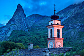 Church of Chiappera, illuminated, with rock spire Rocca Castello in background, Chiappera, Val Maira, Cottian Alps, Piedmont, Italy