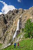 Mann und Frau beim Wandern steigen zum Rifugio Stroppia auf, Wasserfall Cascata Stroppia im Hintergrund, Val Maira, Cottische Alpen, Piemont, Italien