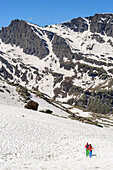 Mann und Frau beim Wandern steigen durch Schnee zum Refuge Viso ab, Giro di Monviso, Monte Viso, Monviso, Cottische Alpen, Frankreich