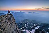 Mann beim Bergsteigen steht auf Felsabsatz und blickt ins Tal, Viso Mozzo, Giro di Monviso, Monte Viso, Monviso, Cottische Alpen, Piemont, Italien