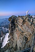 Two persons hiking standing at dawn at summit of Viso Mozzo, Viso Mozzo, Giro di Monviso, Monte Viso, Monviso, Cottian Alps, Piedmont, Italy