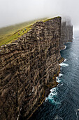 Three mountainbikers ride their bikes along the cliff Trælanípa close by lake Leitisvatn high above the Atlantic ocean, Vagar, Faroe Islands