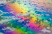 Aerial view of clouds below, at 10,000 meters, photographed from a regular commercial flight. The rainbow of colours is due to light refraction.