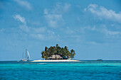 Blick auf eine Insel, groß genug für eine Hütte und ein paar Dutzend Palmen. Sie wird von einem Segelboot angefahren und rechts von einem kleinen Motorboot flankiert, San Blas-Inseln, Panama, Mittelamerika