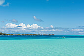 Ein kleines Motorboot kreuzt aus dunklerem tieferem Wasser in das hellere blaugrüne flachere Wasser, im Hintergrund Überwasser Bungalows auf Pfählen von einem Luxusresort, Bora Bora, Gesellschaftsinseln, Französisch-Polynesien, Südpazifik