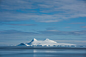 View of an island with two mountain peaks beneath a blue sky streaked with thin clouds, Wilhelmina Bay, Antarctic Peninsula, Antarctica