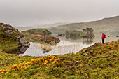 Eine Wanderin blickt auf einen See, Inverpolly Nature Reserve, Highlands, Schottland, Großbritannien