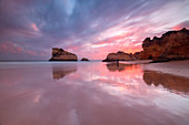 Sunset on cliffs and sandy beach surrounded by the clear sea Praia Dos Tres Irmaos Portimao Algarve Portugal Europe