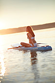 Junge Frau sitzt auf einem SUP Board, Starnberger See, Bayern, Deutschland