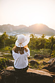 Woman wearing straw hat sitting on rock at sunset on Phi Phi Islands, Thailand