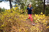 Young woman trail running in forest in autumn, Jackson, Wyoming, USA