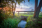 Bridge leads over small stream in the pasture in the morning mood