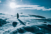 People walking across sunny, windy, snow covered landscape, Reykjadalur, Iceland