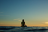 Surferin sitzt auf Surfbrett auf dem Meer bei Sonnenuntergang