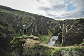 Young man standing on cliff above canyon in Kirkjub?jarklaustur, Iceland
