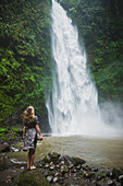 Woman standing by waterfall in Bali, Indonesia