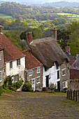 Klassische englische Häuschen neben der gepflasterten Straße von Gold Hill, Shaftesbury, Dorset, England, Großbritannien, Europa