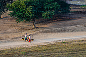 People carrying baskets on dirt path in rural landscape, Myanmar, Burma