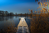 View of a frozen pond with a footbridge in the foreground. Das Blaue Land, Murnau am Staffelsee, Bavaria, Germany