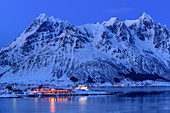 Beleuchtetes Slidpollnes und verschneite Berge spiegeln sich in Fjord, Lofoten, Nordland, Norwegen