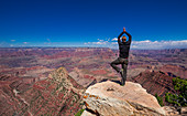 Man in yoga pose on rock on the south rim of the Grand Canyon at sun with blue sky, USA