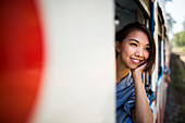 Smiling young woman riding on a train, looking out of window.