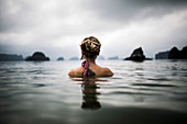 Rear view of woman with blond braided hair wading into the ocean.