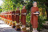 Row of Buddhist monk statues with red robes and alms bowls in the gardens of the Buddhist Temple at Siem Reap