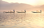 Intha 'leg rowing' fishermen at sunset on Inle Lake who row traditional wooden boats using their leg and fish using nets stretched over conical bamboo frames, Inle Lake, Myanmar (Burma), Southeast Asia