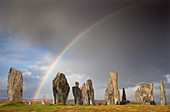 Steinkreise von Callanish im Sonnenlicht mit einem Regenbogen, der sich über den Himmel im Hintergrund wölbt, nahe Carloway, Isle of Lewis, Äußere Hebriden, Schottland, Vereinigtes Königreich, Europa