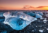 Gebrochenes Eis von angespülten Eisbergen am schwarzen Strand von Jokulsarlon bei Sonnenuntergang, Jokulsarlon, Südostisland, Island, Polarregionen