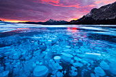 Bubbles and Cracks in the Ice with Kista Peak in the Background at Sunrise, Abraham Lake, Alberta, Canada, North America