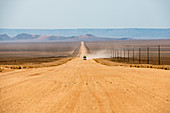 Ein Jeep auf einer langen Sandstraße im Süden Namibias hinterlässt eine Staubspur in Namibia, Afrika
