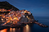 Bucht in Cinque Terre mit Dorf Manarola am Abend mit Lichtern, Italien\n