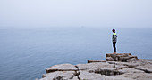 Frau mit Blick auf Meer an den steilen Klippen von Peniche, neben dem Fortaleza de Peniche, Portugal\n
