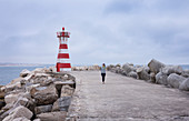 Woman on breakwater and breakwater at the lighthouse of the port of Peniche, Portugal