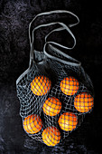 Orangen im grauen Netzbeutel auf schwarzem Hintergrund