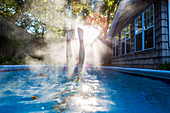 Teenager-Mädchen schwimmt in einem Pool, taucht in warmes Wasser, Dampf steigt auf