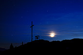 Summit cross of the Jochberg at night with clouds, stars and moon