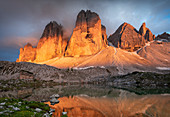 Dramatic Alpine glow of the Three Peaks with reflection in mountain lake at sunset, South Tyrol