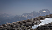 Woman hikes over rock edge, mountains of the Dolomites in the background, with snow field, Cinque Torri South Tyrol