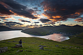 Wanderer vor dem Fjord und der Stadt Vetsmanna unter buntem Sonnenuntergang, Streymoy, Färöer, Dänemark