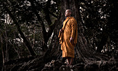 Siem Reap, Cambodia - January 19, 2011: A monk in his orange robe is standing next to an old tree inside the Angkor Wat complex.