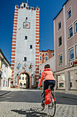 Frau beim Radfahren fährt durch Stadttor von Mühldorf, Mühldorf, Benediktradweg, Oberbayern, Bayern, Deutschland