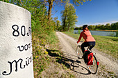 Frau fährt mit Rad am Inn entlang, alter Kilometerstein im Vordergrund, Inn, Benediktradweg, Oberbayern, Bayern, Deutschland