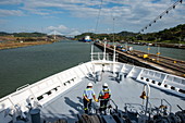 View of the bow of an expedition cruise ship with two workers from the Panama Canal while the ship leaves the Pedro Miguel locks, with the Centennial Bridge visible in the distance, near Panama City, Panama, Central America,